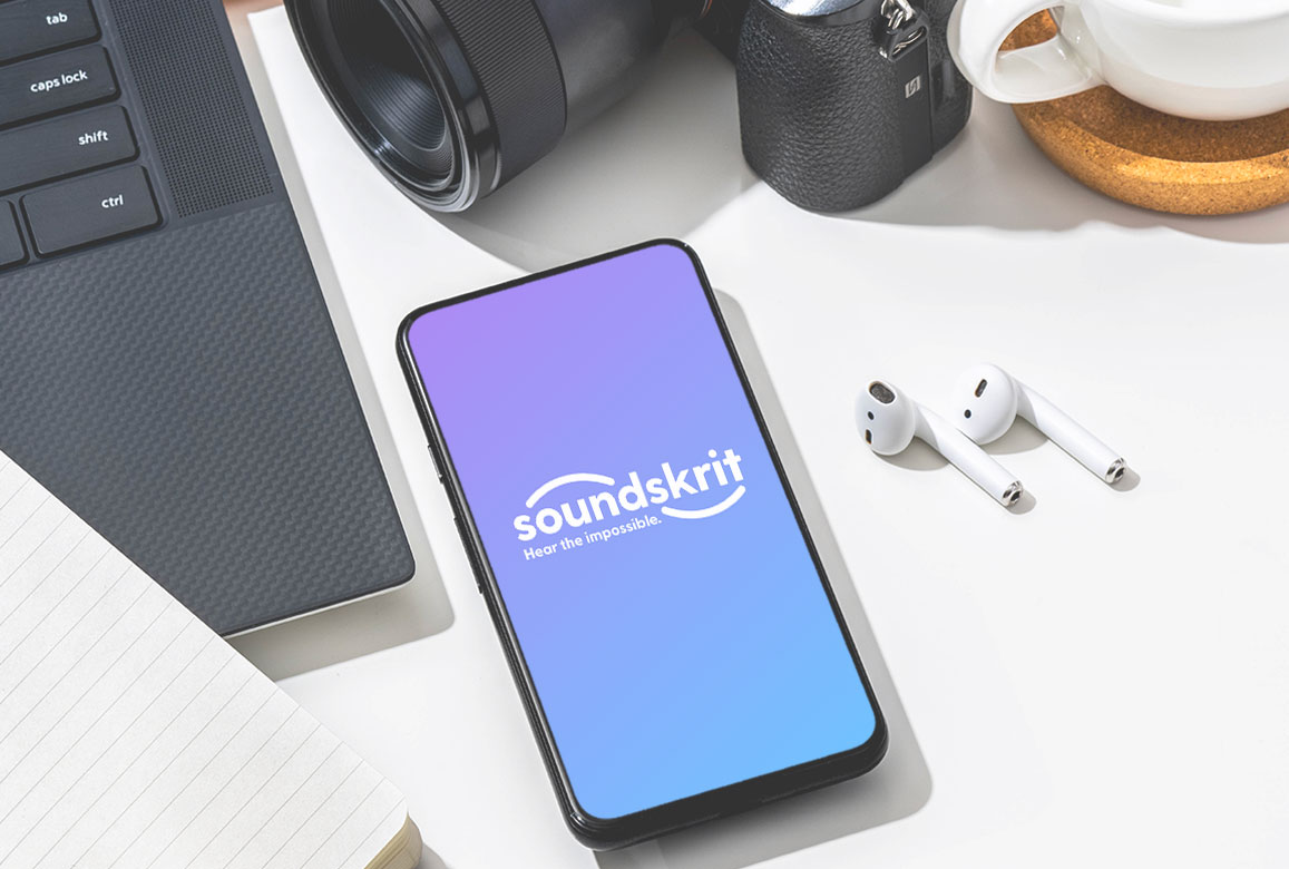 smartphone avec logo Soundskrit sur l'écran, écouteurs airpods, appareil photo dslr et clavier sur le bureau